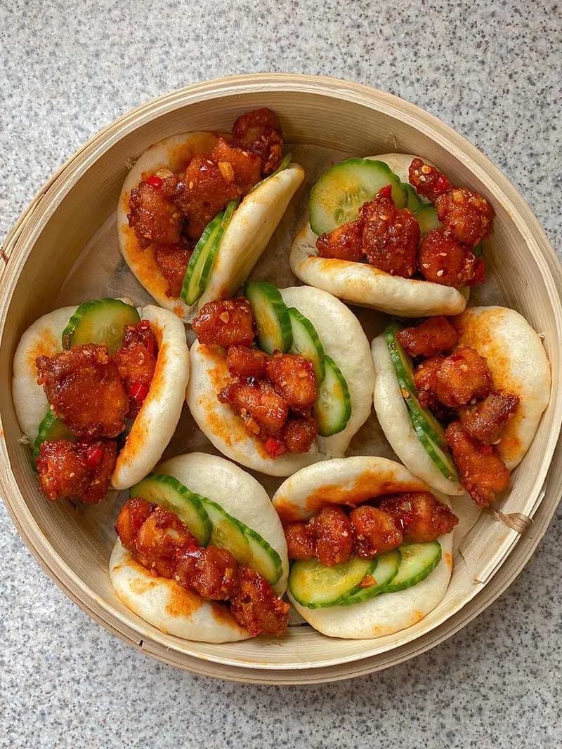 Steamed bao buns stacked beside a bamboo steamer