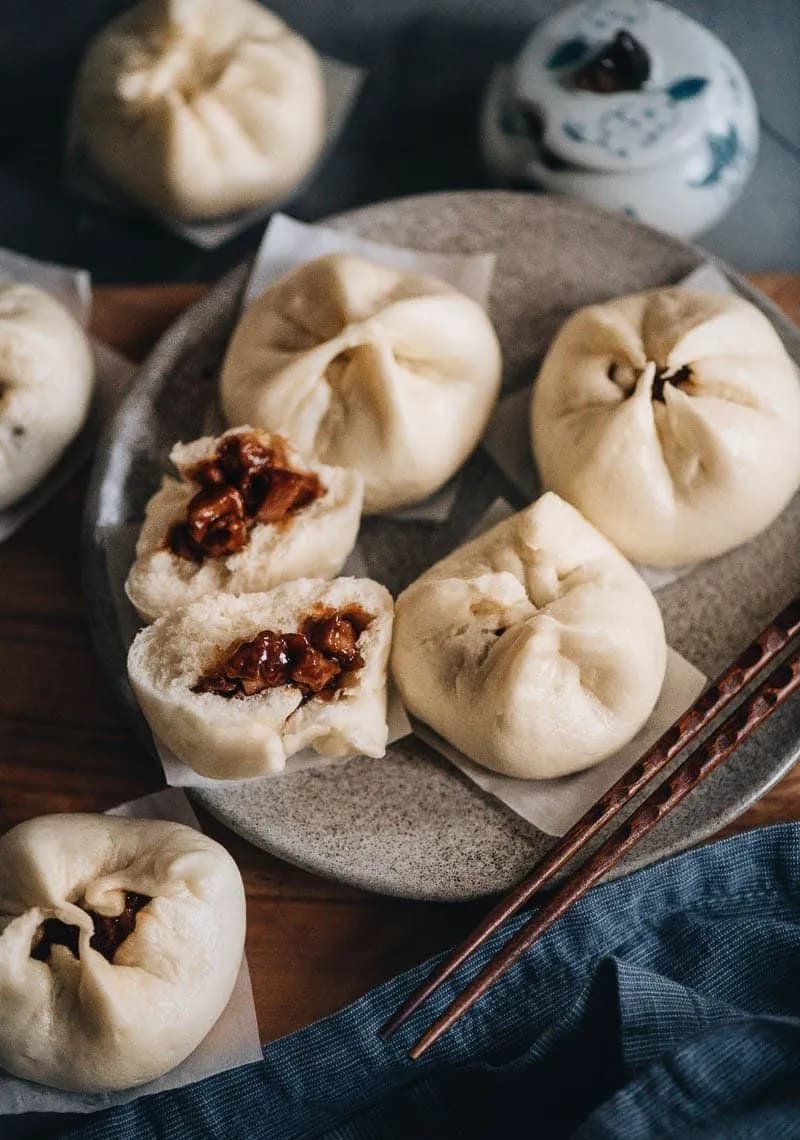 Two soft white steamed bao in a bamboo basket