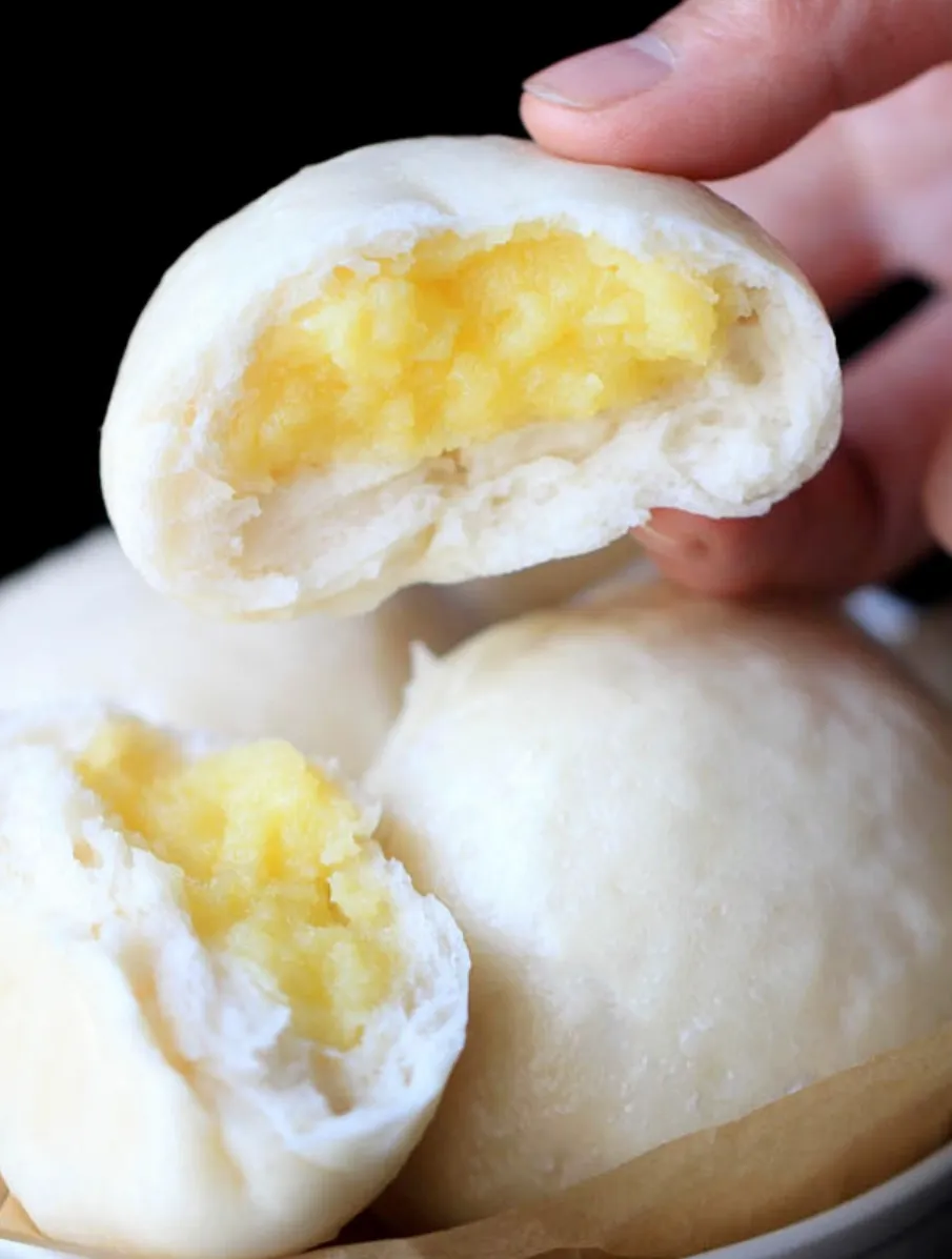 A steamed custard bun torn open, golden custard inside