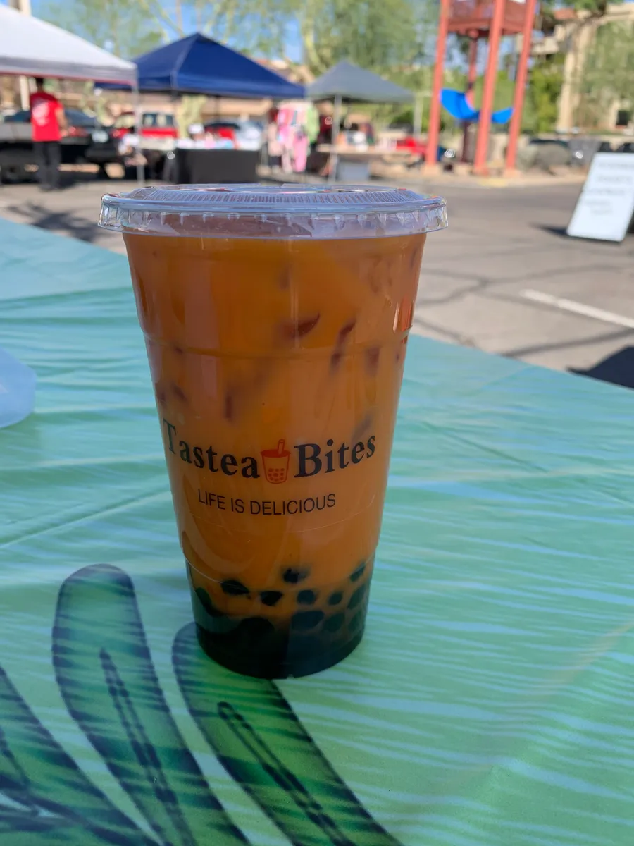 A Tastea Bites cup of classic milk tea with boba, on the market table