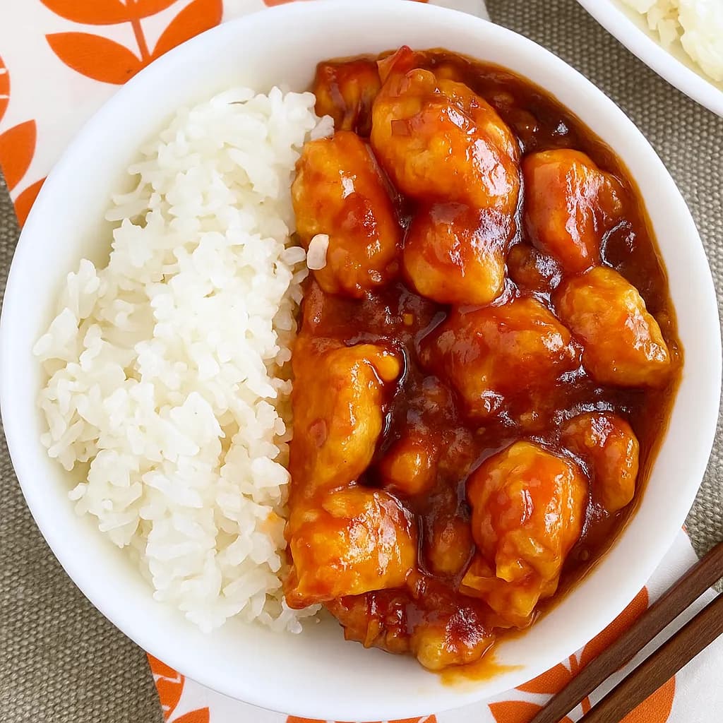 A bowl of glossy orange chicken over white steamed rice