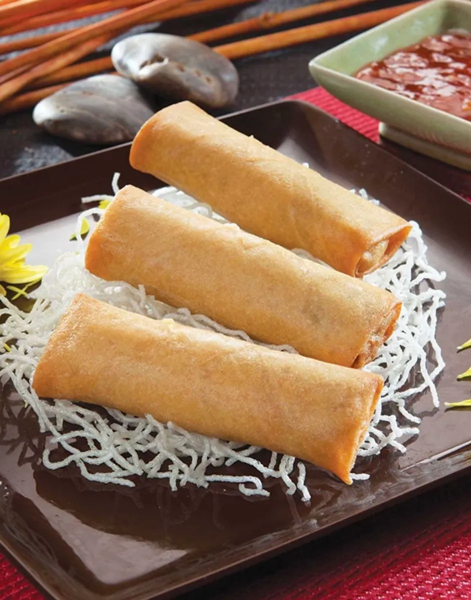 Three golden spring rolls stacked on crispy noodles