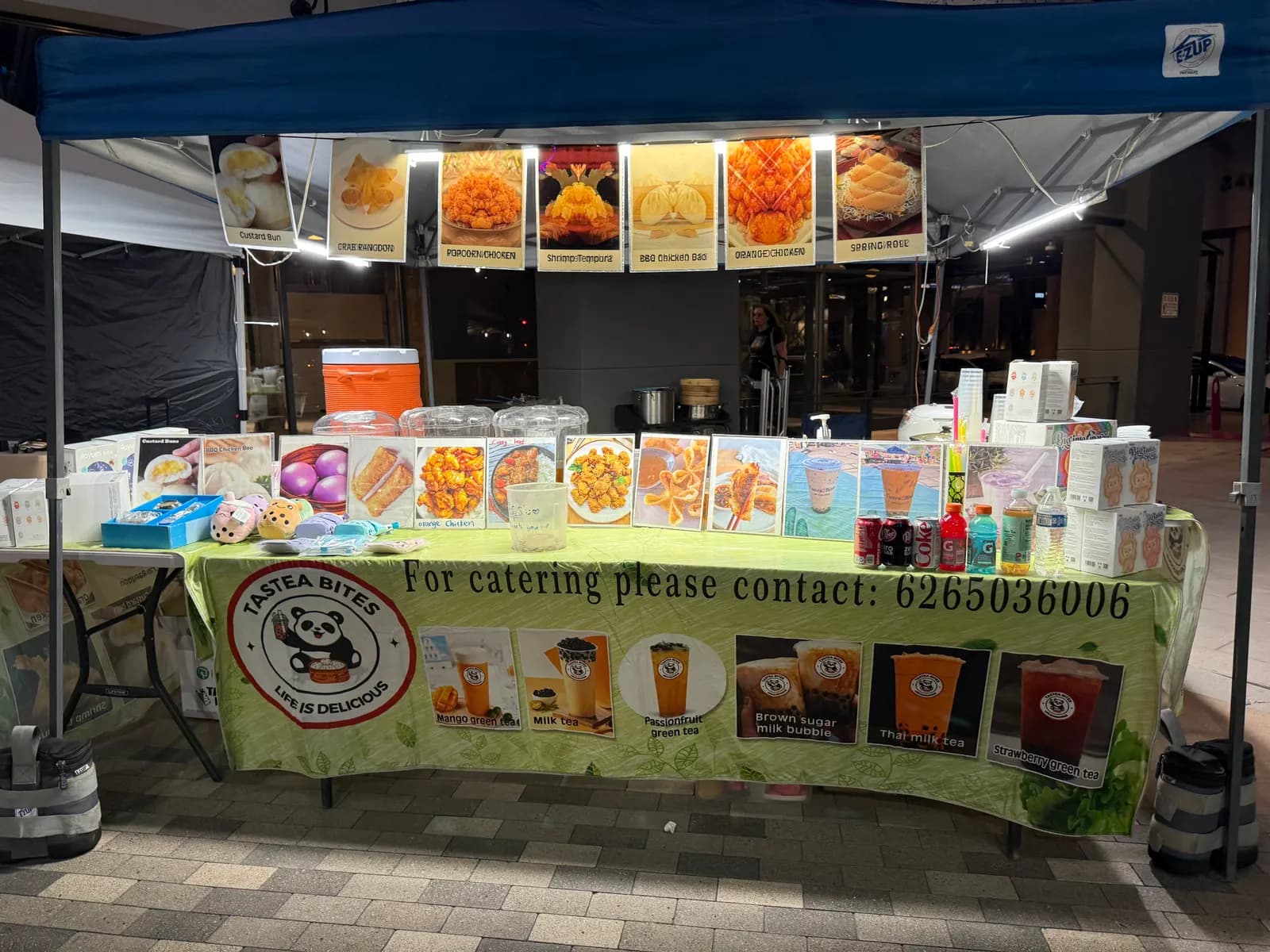 The Tastea Bites stall serving at an evening event, milk tea menu lit up under the canopy lights